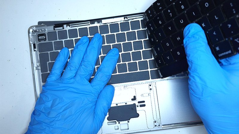 technician taking off broken macbook keyboard for replacement with new original one